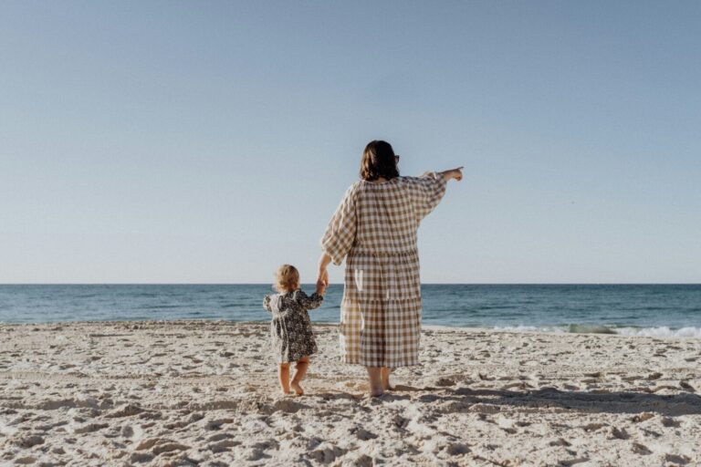 woman holding toddler girl's hand at the beach