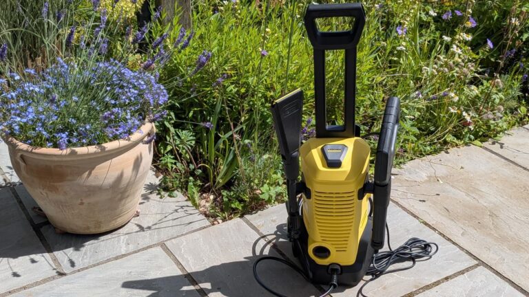 The K&auml;rcher K3 eco!Booster pressure washer on a garden patio in front of some plants and flowers